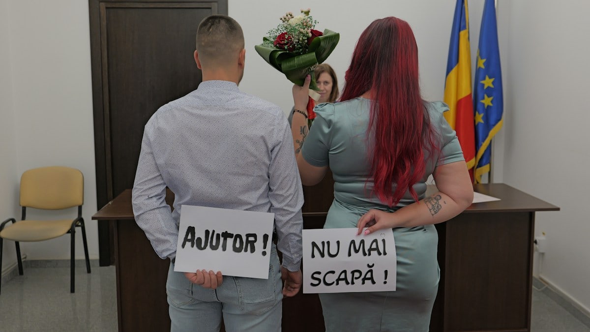 A man and a woman holding signs reading AJUTOR and NU MAI SCAPĂ